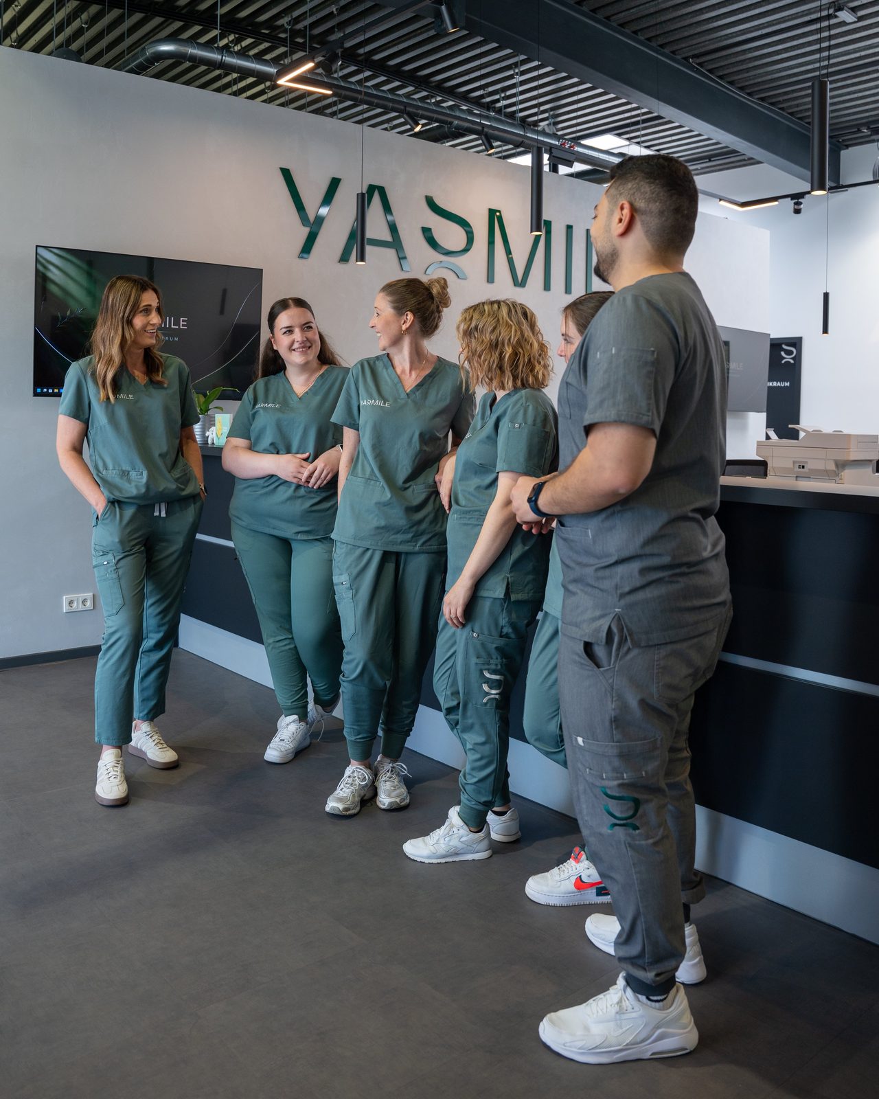 Das YASMILE-Team im Gespräch vor der Praxiswand mit dem YASMILE-Schriftzug